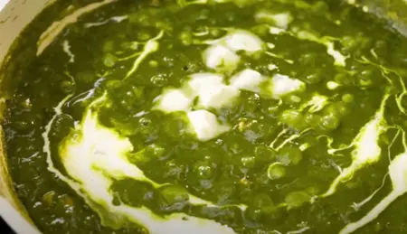 Stirring in curd to the spinach and corn mixture while cooking Palak Corn Ki Sabji.