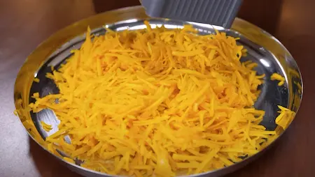 Peeling and grating red pumpkin for Kaddu Ka Halwa recipe.