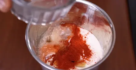 Blending diced tomatoes, rice flour, suji, ginger, and red chili powder with water.