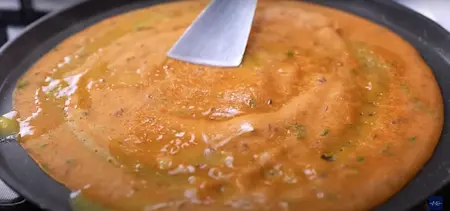 Adding butter and grated cheese to the cooking tomato dosa.