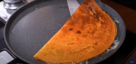 Folding the crispy tomato dosa with melted cheese and serving hot.