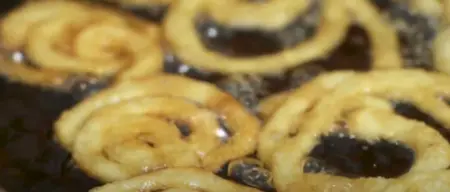 Spirals of jalebi batter being fried in hot oil to a crispy golden brown.