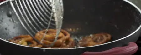 Crispy jalebis being soaked in hot sugar syrup for a sweet coating.