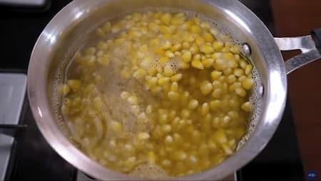 Corn kernels being boiled in a deep pot to prepare for crispy corn.