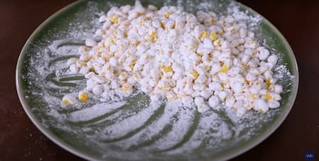 Corn kernels being coated in a mixture of cornflour and spices for frying.