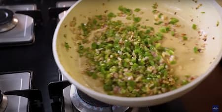 Chopped garlic, ginger, capsicum, and onion being stir-fried in a pan.