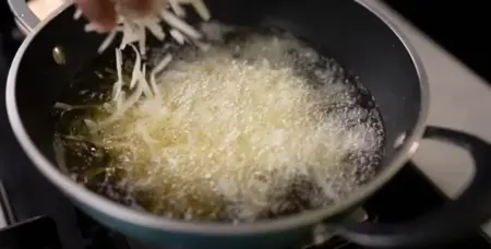 Grated potatoes being deep-fried until crispy and golden brown.