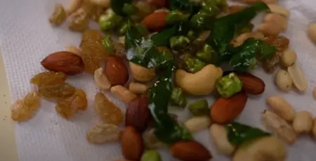 Fried almonds, cashew nuts, peanuts, raisins, green chilies, and curry leaves being added to the seasoned potatoes.