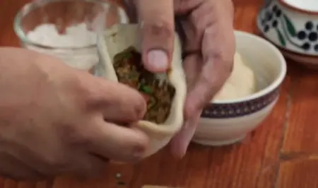 The rolled dough ball being flattened with keema filling visible inside.