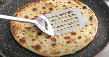 The paratha cooking on a tawa with golden brown spots visible.