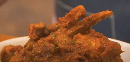 A bowl of aromatic Mutton Curry garnished with chopped coriander and served with rice.