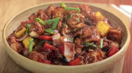 Crispy chilli paneer garnished with spring onions and coriander leaves, served on a plate.