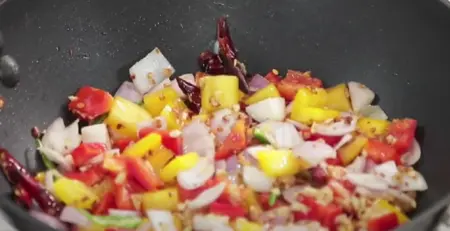 Stir-frying garlic, chilies, peppers, onions, and ginger in a wok.