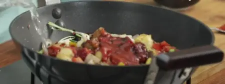 Crispy paneer being coated with sauces and vegetables in a wok.