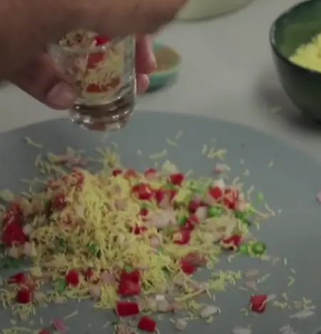  Base salad being mixed with onion, tomatoes, coriander, sev, and spices.