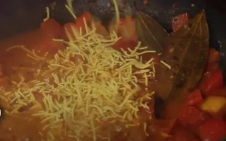 Mixing sev into the thickened tomato gravy for Sev Tamatar Nu Shak.