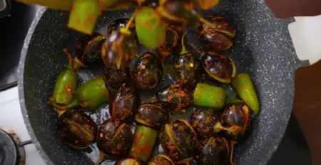 Sautéing marinated eggplants and Bhavnagri mirch in a pan before adding the gravy.