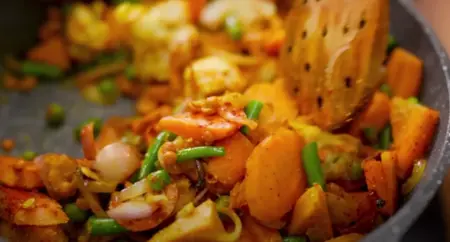 Spices and vegetables being mixed and cooked together.