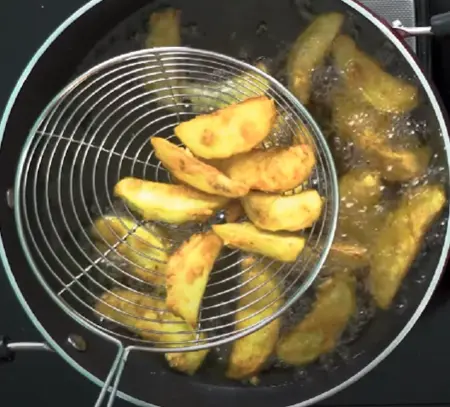 Golden brown crispy potato fries being removed from oil with a slotted spoon.