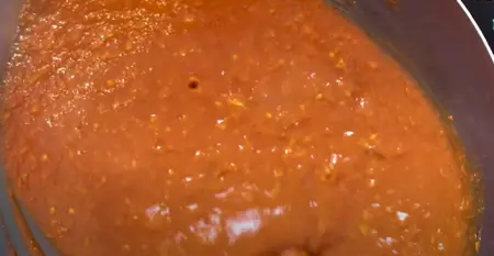 Schezwan sauce being prepared in a wok with chopped garlic, green chillies, ginger, and red chilli paste.