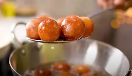 Golden brown Gulab Jamun balls frying in oil.