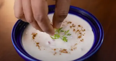 Pomegranate raita being mixed with spices and garnished with fried garlic.