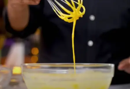 Thick besan batter being mixed with carom seeds, red chilli powder, salt, and turmeric.