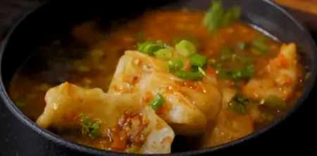 Serving the steamed momos with hot vegetable soup and garnishes.