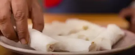 Spring roll sheet being filled with vegetable mixture and folded for frying