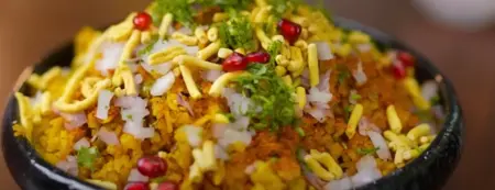 Cooking Indori Poha with aromatic spices and garnishing it with pomegranate seeds, Ratlami sev, and onions.