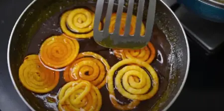 Frying Jalebi in hot ghee until golden brown for a crispy and sweet treat.