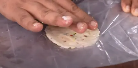 Rolling out the Nippat dough thinly between plastic sheets and cutting into circular shapes.