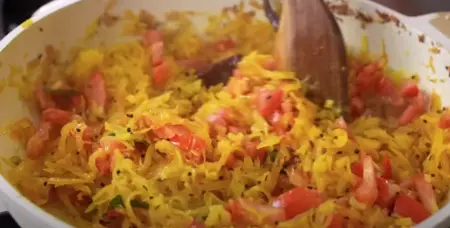 Adding tomatoes, turmeric, and salt to the softened papaya in the pan.