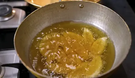 Shaped dough pieces frying in hot oil in a deep pan, turning golden brown.