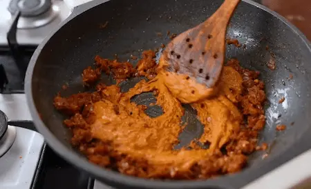 Adding spiced curd mixture to simmering gravy.