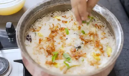 Saffron milk and toppings being added to the biryani