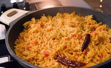 Rice mixed with vegetables and spices, cooking in a pan