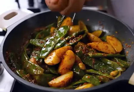 Cooking sem and potatoes in achari masala