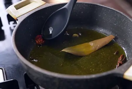 Tempering whole spices in mustard oil for dum aloo in Aloo Dum Muri Ghugni recipe