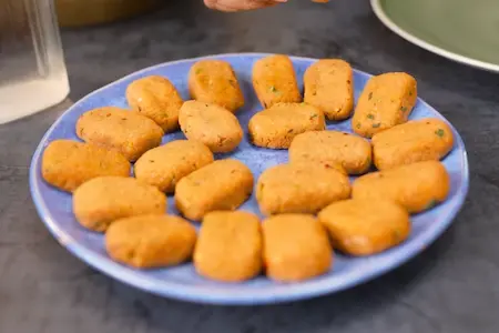 Shaped nuggets being coated with crushed cornflakes