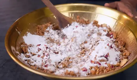 Adding powdered sugar and dried rose petals to Pinni Laddu mixture