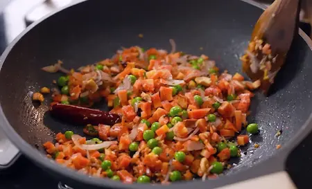 Green peas, diced carrots, and spices being mixed in a pan