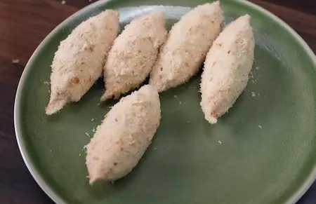 Coating Dahi Ke Sholey recipe rolls with slurry and breadcrumbs before frying