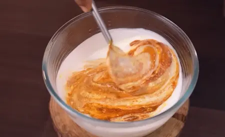 Step 6: Mixing spiced masala into whisked curd for Dahi Baingan