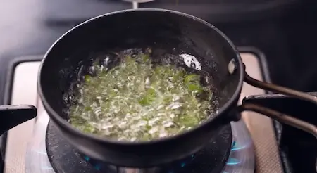 Pouring hot mustard tadka with green chilli and curry leaves over Koshimbir salad