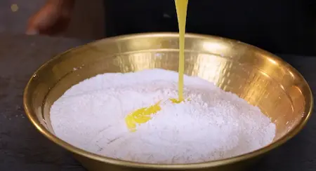 A mixing bowl with flour, sugar, coconut, ghee, and other ingredients combined for the shakarpara dough.