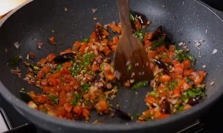 Vegetable mixture with onions, tomatoes, and chillies cooking in a pan.