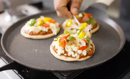 Assembling mini pizzas with sauce, toppings, and cheese on the tawa.