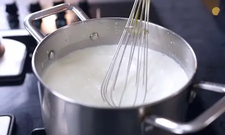 adding cornflour slurry and milk powder to boiling milk for homemade dahi