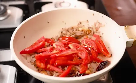 Cooking sliced onions and tomatoes in a pan until they become soft and form a rich masala base.